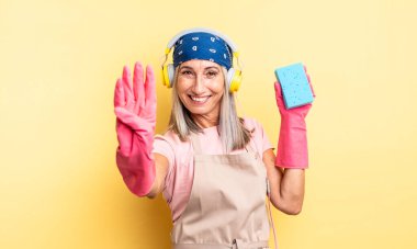 Orta yaşlı güzel bir kadın gülümsüyor ve arkadaş canlısı görünüyor, dört numarayı gösteriyor. Temizleyici.