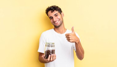 İspanyol yakışıklı adam kendini gururlu hissediyor, başparmağıyla olumlu gülümsüyor. Kahve şişesi.