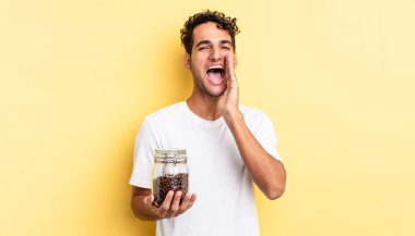 İspanyol yakışıklı adam kendini mutlu hissediyor, elleri ağızının yanında bağırıyor. Kahve şişesi.