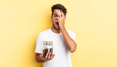 İspanyol yakışıklı adam şok olmuş, korkmuş ya da korkmuş görünüyor. Yüzü elle kapatılmış. Kahve şişesi.