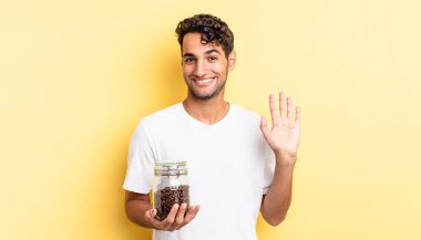 İspanyol yakışıklı adam mutlu bir şekilde gülümsüyor, el sallıyor, seni selamlıyor ve selamlıyor. Kahve şişesi.