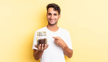 İspanyol yakışıklı adam neşeyle gülümsüyor, mutlu hissediyor ve bir tarafı işaret ediyor. Kahve şişesi.