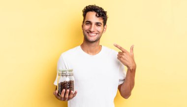 İspanyol yakışıklı adam kendine güvenerek gülüyor ve kendi gülüşüne işaret ediyor. Kahve şişesi.