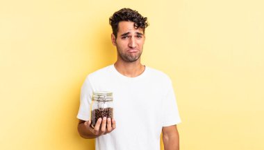 Hispanik yakışıklı adam üzgün ve mızmız, mutsuz bir bakışla ağlıyor. Kahve şişesi.