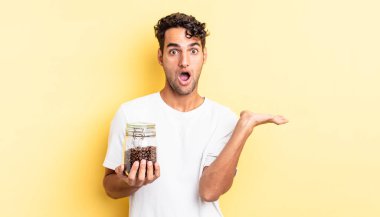 İspanyol yakışıklı adam şaşırmış ve şok olmuş görünüyor. Çenesi düşmüş ve elinde bir nesne var. Kahve şişesi.