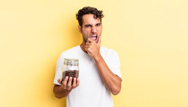 Ağzı ve gözleri açık, eli çenesinde İspanyol yakışıklı bir adam. Kahve şişesi.