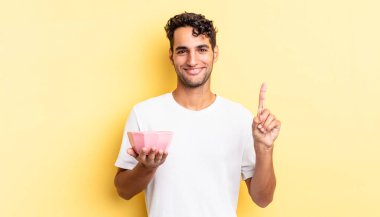 İspanyol yakışıklı adam gülümsüyor ve arkadaş canlısı görünüyor, bir numarayı gösteriyor. boş kase kavramı