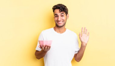 İspanyol yakışıklı adam mutlu bir şekilde gülümsüyor, el sallıyor, seni selamlıyor ve selamlıyor. boş kase kavramı