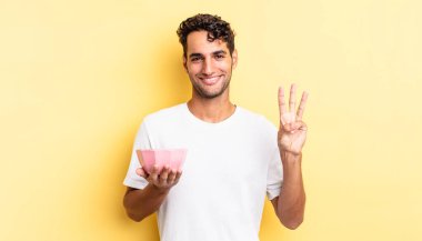 İspanyol yakışıklı adam gülümsüyor ve arkadaş canlısı görünüyor, üç numarayı gösteriyor. boş kase kavramı