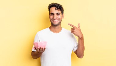 İspanyol yakışıklı adam kendine güvenerek gülüyor ve kendi gülüşüne işaret ediyor. boş kase kavramı