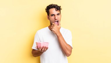 Ağzı ve gözleri açık, eli çenesinde İspanyol yakışıklı bir adam. boş kase kavramı