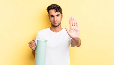 İspanyol yakışıklı adam ciddi görünüyor. Avuç içi gösteriyor. Durdurma hareketi yapıyor. Kahve termosu kavramı