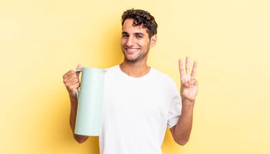 İspanyol yakışıklı adam gülümsüyor ve arkadaş canlısı görünüyor, üç numarayı gösteriyor. Kahve termosu kavramı