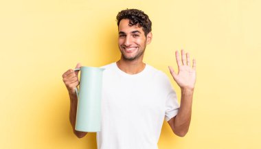 İspanyol yakışıklı adam mutlu bir şekilde gülümsüyor, el sallıyor, seni selamlıyor ve selamlıyor. Kahve termosu kavramı