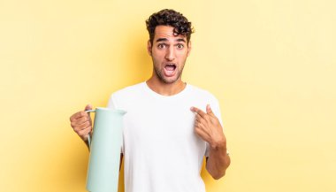 İspanyol yakışıklı adam şok olmuş ve ağzı açık, kendini işaret ederek şaşırmış görünüyor. Kahve termosu kavramı