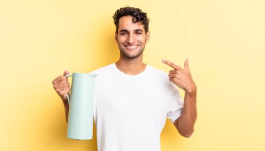 İspanyol yakışıklı adam kendine güvenerek gülüyor ve kendi gülüşüne işaret ediyor. Kahve termosu kavramı