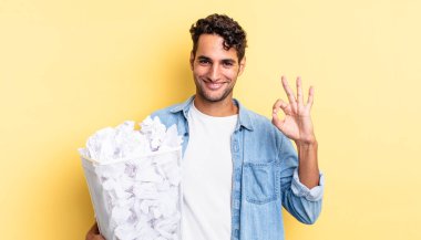 İspanyol yakışıklı adam kendini mutlu hissediyor, iyi bir jestle onaylıyor. kağıt toplar çöp konsepti