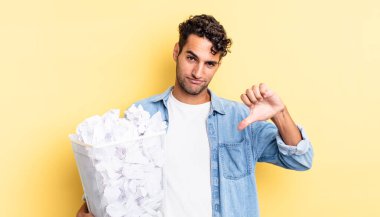 Latin asıllı yakışıklı adam kızgın, baş parmağını kaldırıyor. kağıt toplar çöp konsepti