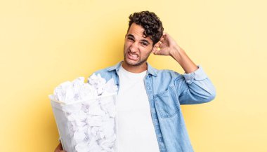 İspanyol yakışıklı adam kendini stresli, endişeli ya da korkmuş hissediyor, elleri başının üstünde. kağıt toplar çöp konsepti