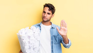 İspanyol yakışıklı adam ciddi görünüyor. Avuç içi gösteriyor. Durdurma hareketi yapıyor. kağıt toplar çöp konsepti