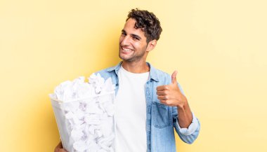 İspanyol yakışıklı adam kendini gururlu hissediyor, başparmağıyla olumlu gülümsüyor. kağıt toplar çöp konsepti