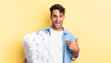 İspanyol yakışıklı adam mutlu hissediyor ve heyecanla kendini işaret ediyor. kağıt toplar çöp konsepti