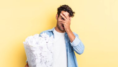 İspanyol yakışıklı adam şok olmuş, korkmuş ya da korkmuş görünüyor. Yüzü elle kapatılmış. kağıt toplar çöp konsepti
