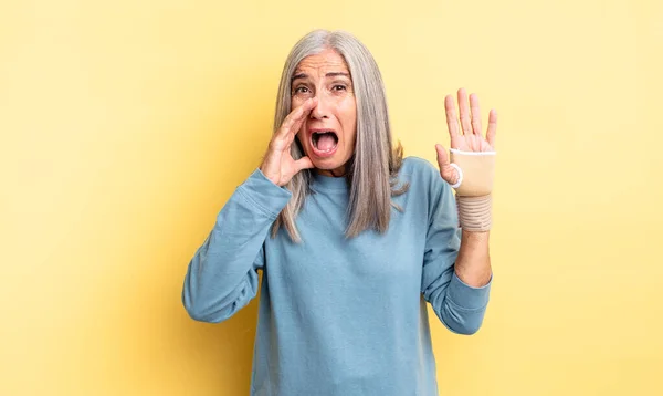 中年の女性は幸せを感じ口の横に手で大きな声を出す 手の包帯の概念 — ストック写真