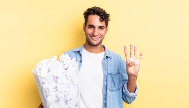 İspanyol yakışıklı adam gülümsüyor ve arkadaş canlısı görünüyor, dört numarayı gösteriyor. kağıt toplar çöp konsepti