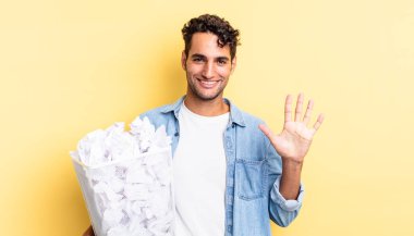 İspanyol yakışıklı adam gülümsüyor ve arkadaş canlısı görünüyor, beş numarayı gösteriyor. kağıt toplar çöp konsepti