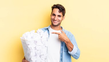 İspanyol yakışıklı adam neşeyle gülümsüyor, mutlu hissediyor ve bir tarafı işaret ediyor. kağıt toplar çöp konsepti