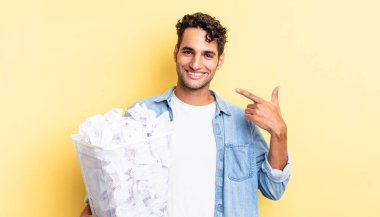 İspanyol yakışıklı adam kendine güvenerek gülüyor ve kendi gülüşüne işaret ediyor. kağıt toplar çöp konsepti