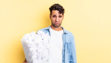 Hispanik yakışıklı adam üzgün ve mızmız, mutsuz bir bakışla ağlıyor. kağıt toplar çöp konsepti