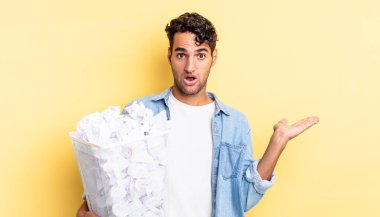 İspanyol yakışıklı adam şaşırmış ve şok olmuş görünüyor. Çenesi düşmüş ve elinde bir nesne var. kağıt toplar çöp konsepti