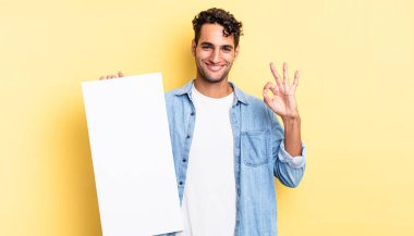 İspanyol yakışıklı adam kendini mutlu hissediyor, iyi bir jestle onaylıyor. boş tuval kavramı