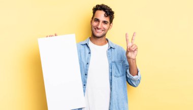 İspanyol yakışıklı adam gülümsüyor ve mutlu görünüyor, zafer ya da barış işareti yapıyor. boş tuval kavramı