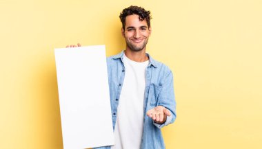 İspanyol yakışıklı adam mutlu bir şekilde gülümsüyor ve bir konsept sunuyor. boş tuval kavramı