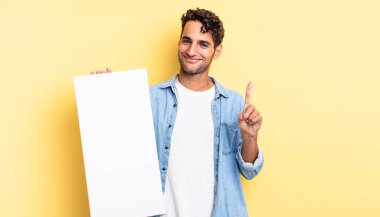 İspanyol yakışıklı adam gülümsüyor ve arkadaş canlısı görünüyor, bir numarayı gösteriyor. boş tuval kavramı