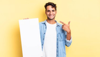 İspanyol yakışıklı adam kendine güvenerek gülüyor ve kendi gülüşüne işaret ediyor. boş tuval kavramı