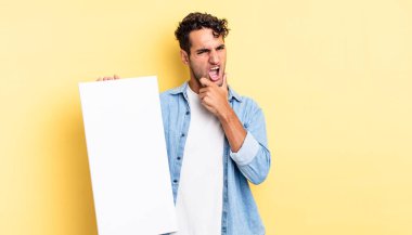 Ağzı ve gözleri açık, eli çenesinde İspanyol yakışıklı bir adam. boş tuval kavramı