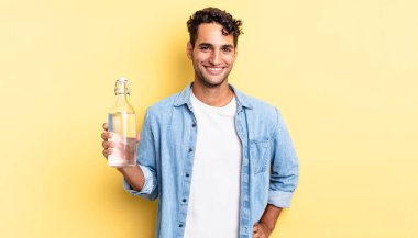 İspanyol yakışıklı adam mutlu bir şekilde gülümsüyor, eli kalçasında ve kendinden emin. su şişesi kavramı