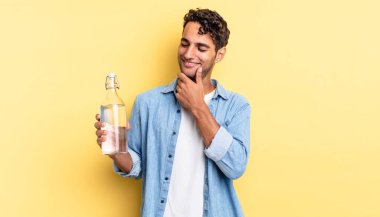 Mutlu, kendine güvenen, elleri çenesinde gülümseyen İspanyol yakışıklı bir adam. su şişesi kavramı