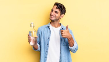 İspanyol yakışıklı adam kendini gururlu hissediyor, başparmağıyla olumlu gülümsüyor. su şişesi kavramı