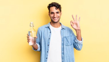 İspanyol yakışıklı adam kendini mutlu hissediyor, iyi bir jestle onaylıyor. su şişesi kavramı