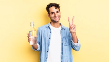 İspanyol yakışıklı adam gülümsüyor ve mutlu görünüyor, zafer ya da barış işareti yapıyor. su şişesi kavramı