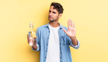İspanyol yakışıklı adam ciddi görünüyor. Avuç içi gösteriyor. Durdurma hareketi yapıyor. su şişesi kavramı