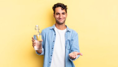 İspanyol yakışıklı adam mutlu bir şekilde gülümsüyor ve bir konsept sunuyor. su şişesi kavramı