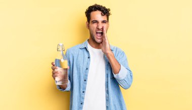 İspanyol yakışıklı adam kendini mutlu hissediyor, elleri ağızının yanında bağırıyor. su şişesi kavramı