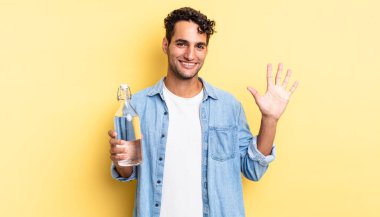 İspanyol yakışıklı adam gülümsüyor ve arkadaş canlısı görünüyor, beş numarayı gösteriyor. su şişesi kavramı