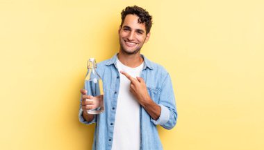 İspanyol yakışıklı adam neşeyle gülümsüyor, mutlu hissediyor ve bir tarafı işaret ediyor. su şişesi kavramı